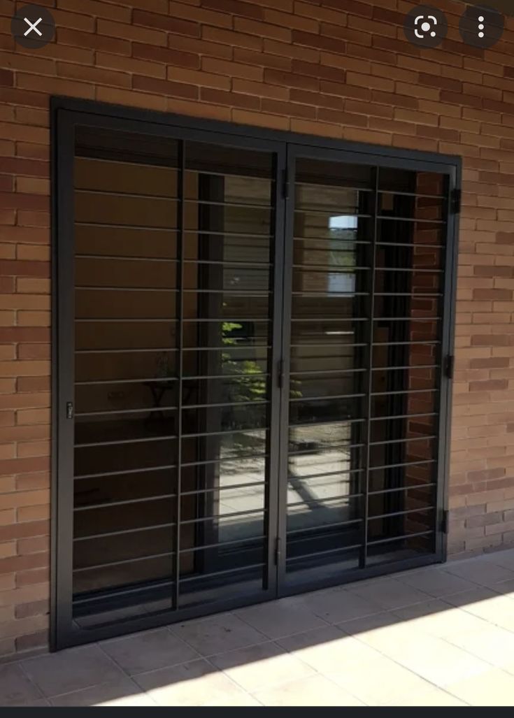 an open sliding glass door in front of a brick building with black bars on it