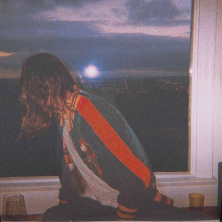 a person sitting on a window sill looking out at the night sky and clouds