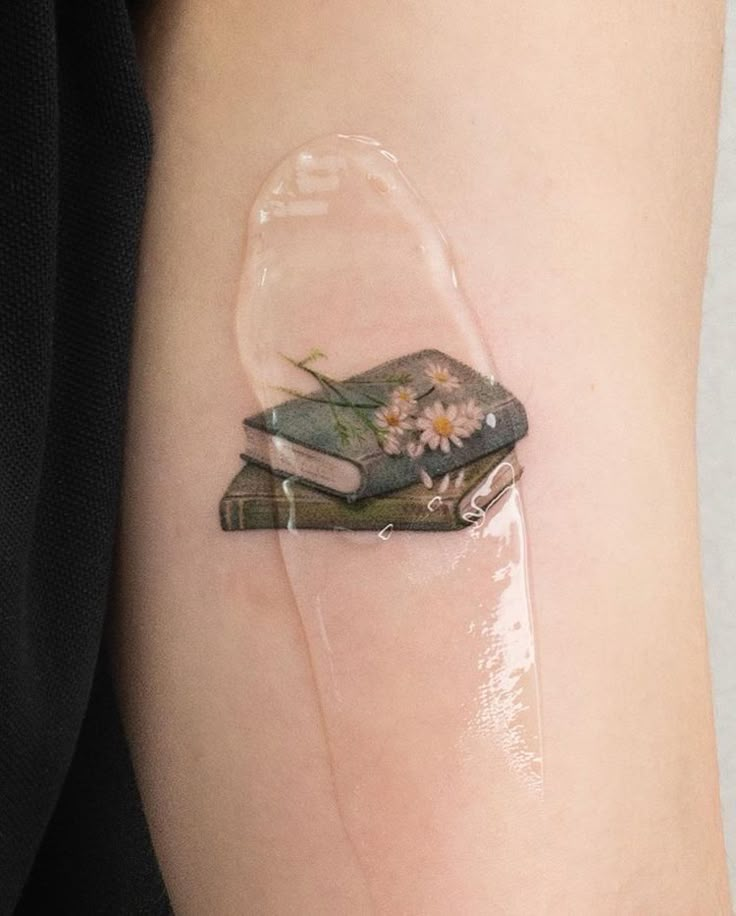 a person with a tattoo on their arm has a book in a glass jar and flowers