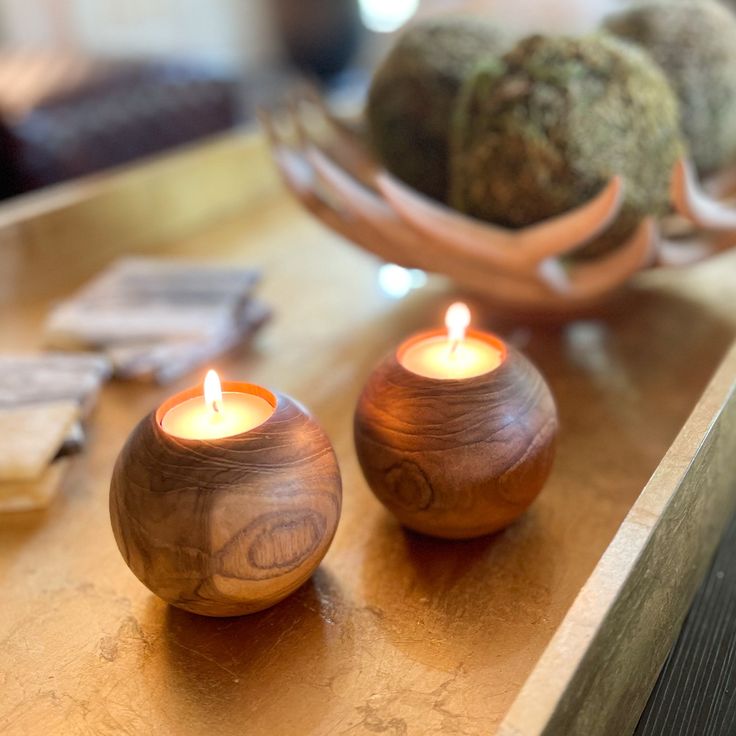 two tea lights sitting on top of a wooden table next to rocks and a bowl