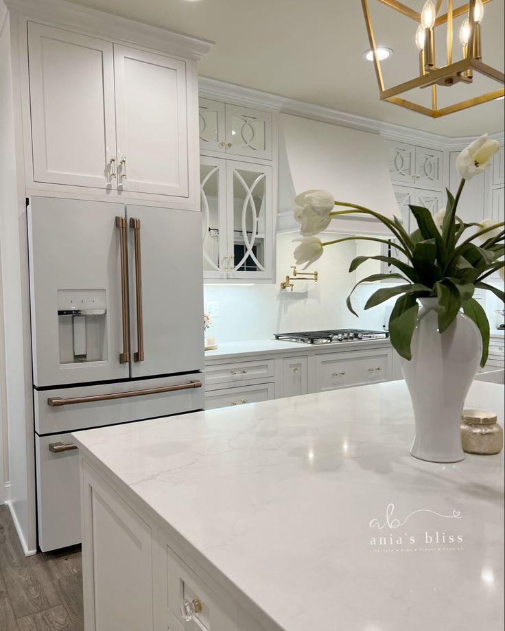 a white kitchen with marble counter tops and gold accents