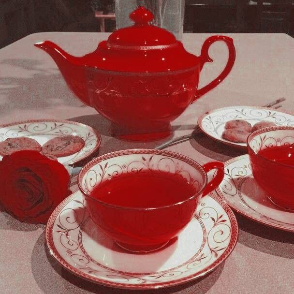 a red tea set sitting on top of a table next to two cups and saucers