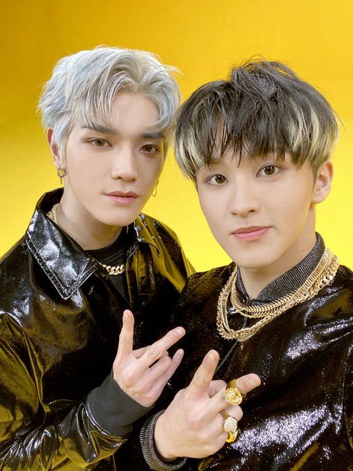 two young men standing next to each other in front of a yellow background with one pointing at the camera