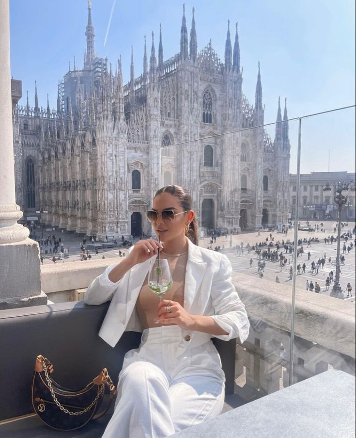 a woman sitting on top of a bench next to a tall building with lots of spires