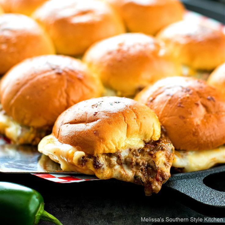 several sliders with cheese and meat are on a plate next to hotdog buns