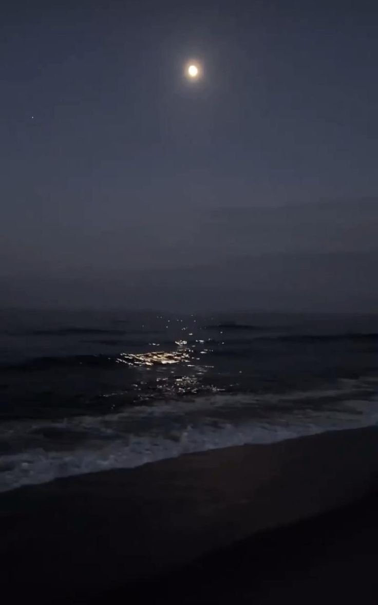 the moon is shining over the ocean at night