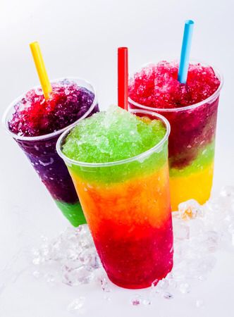 three different colored drinks in plastic cups with straws and ice on white background stock photo