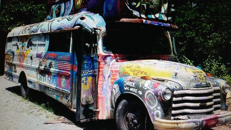 an old bus covered in graffiti sitting on the side of a road next to trees