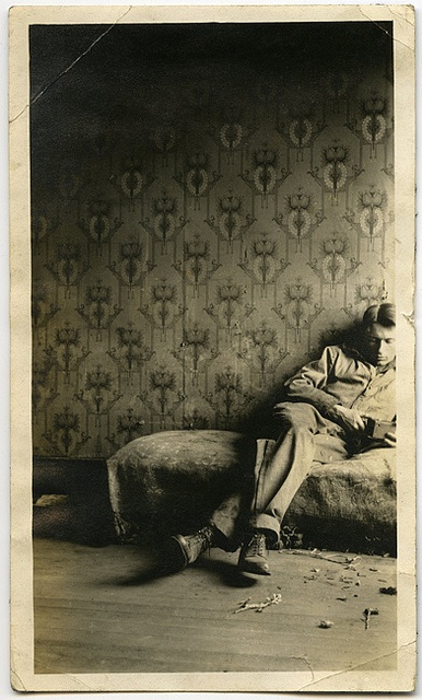 an old black and white photo of a man sitting on a bed in a room