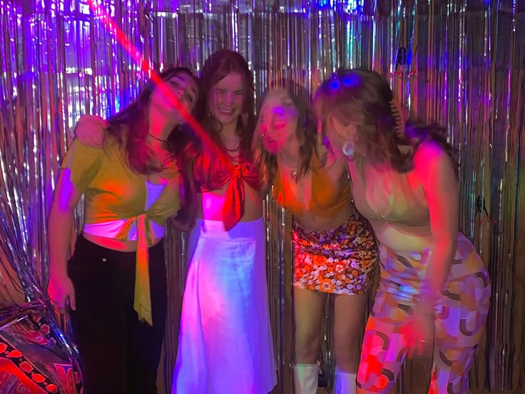 three women standing next to each other in front of a disco curtain with neon lights