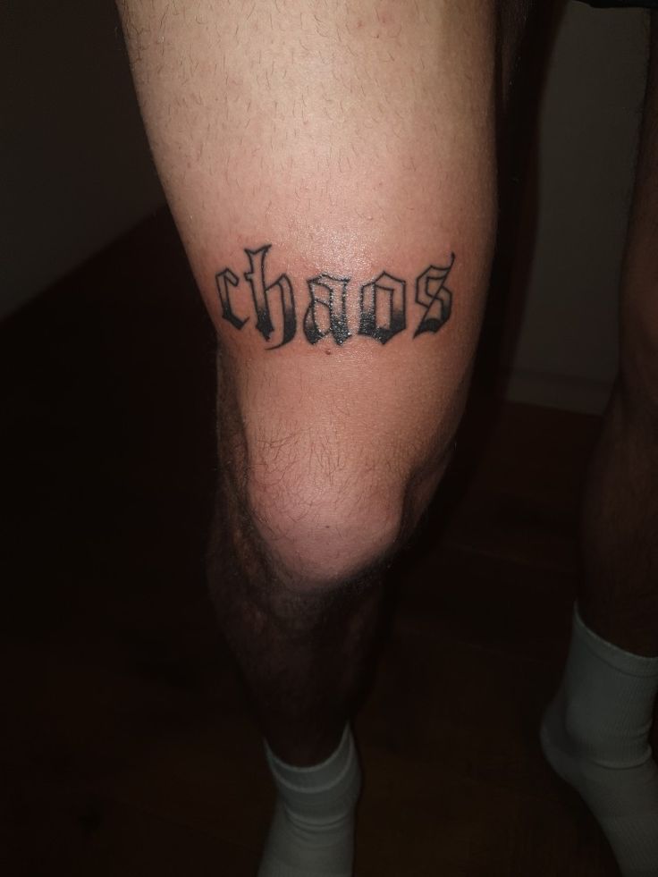 a man's leg with the word chaos tattooed on it, in black ink