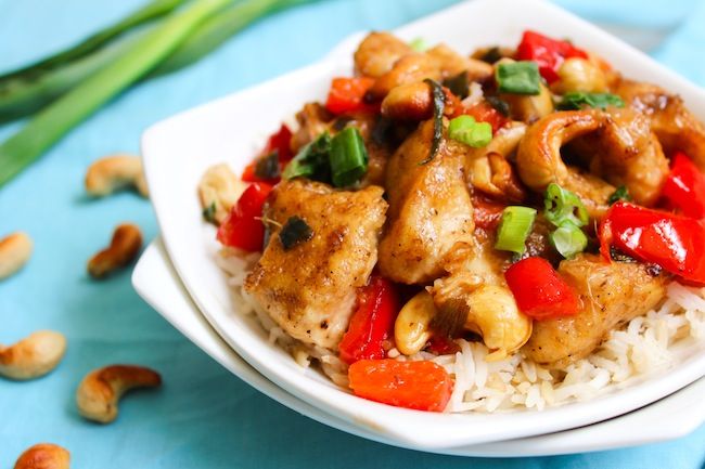 a white plate topped with chicken and vegetables on top of rice next to cashews