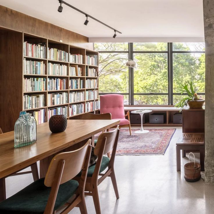 a dining room table with chairs and bookshelves in front of the window that overlooks trees