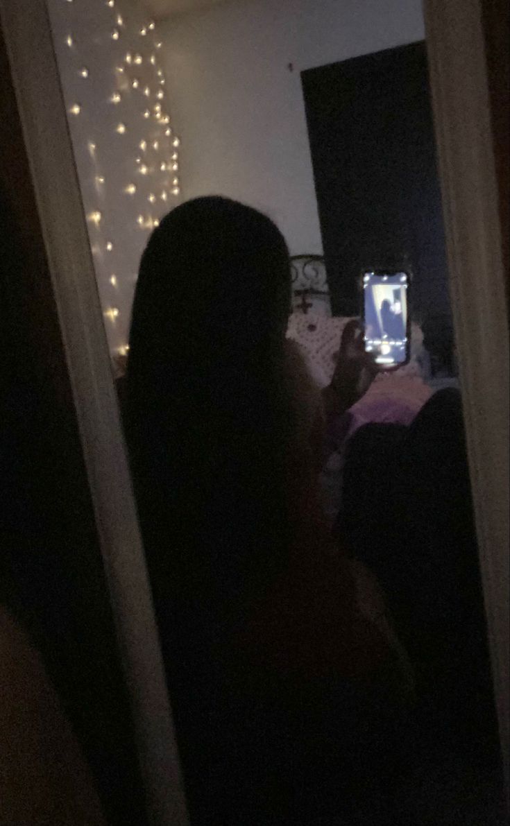 a woman taking a selfie in the mirror with her cell phone at night time