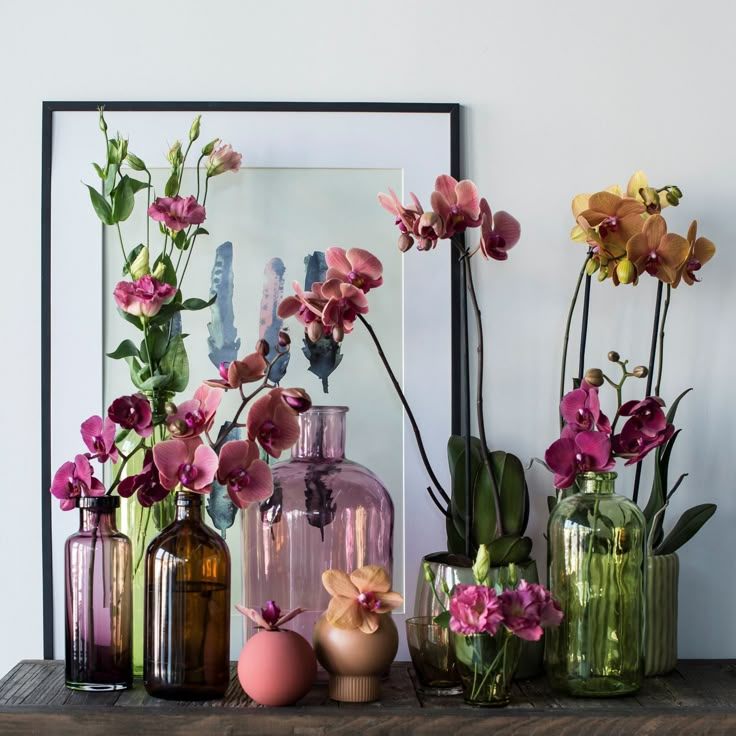 several vases with flowers in them sitting on a shelf next to a framed photograph