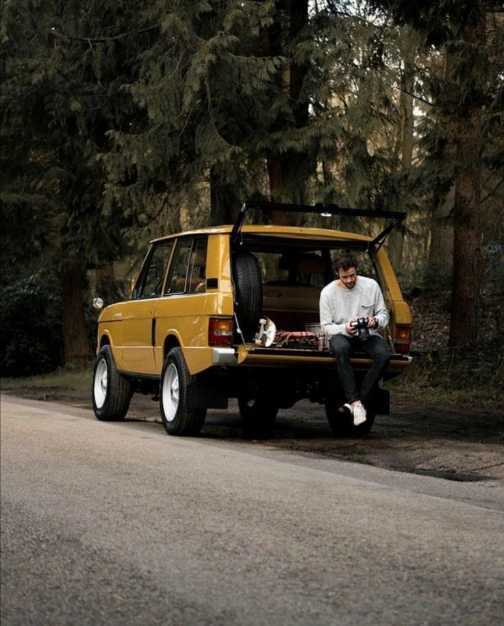 a man sitting on the back of a yellow car with his dog in the trunk