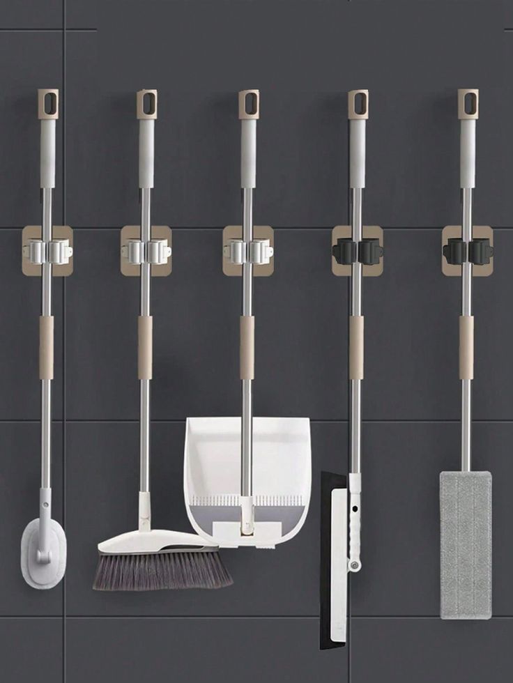 four different types of brooms and mop hooks on a wall with grey tiles