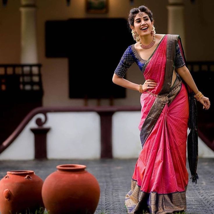 a woman in a pink and grey sari standing next to two clay urns