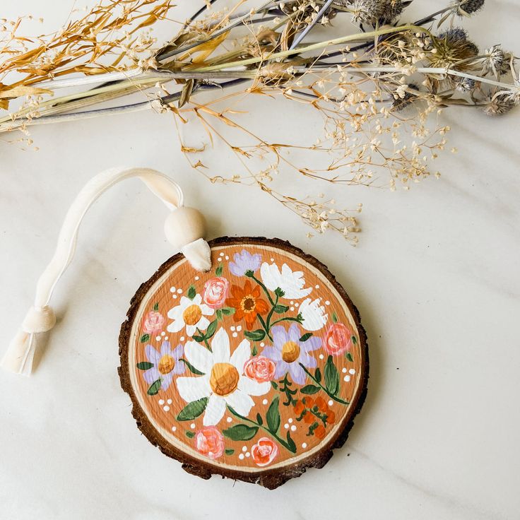 an orange and white flower painted on a wood slice with some dried flowers in the background