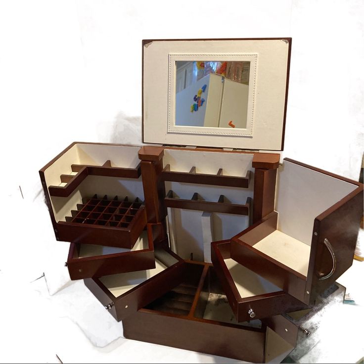 an open jewelry box with several drawers and a mirror on the wall in front of it