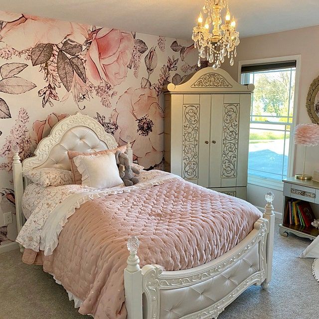 a white bed sitting in a bedroom next to a dresser and window with pink flowers on it