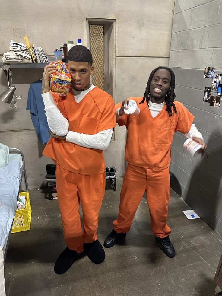 two men dressed in orange prison uniforms are standing next to each other and one is holding a package