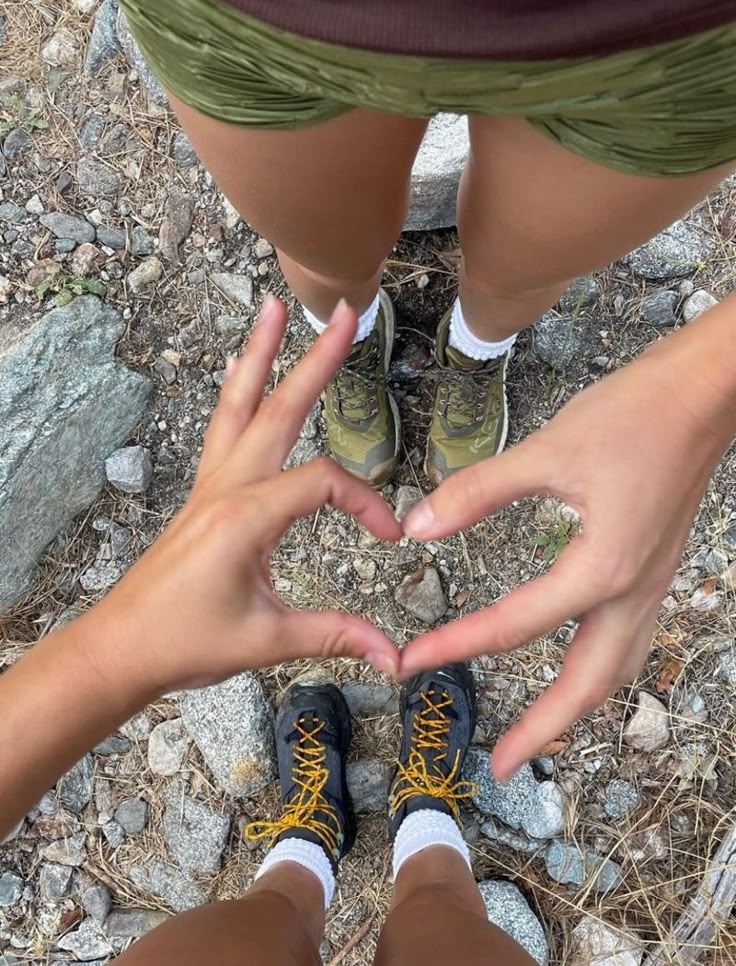 two people making a heart shape with their hands while standing on the ground in front of some rocks