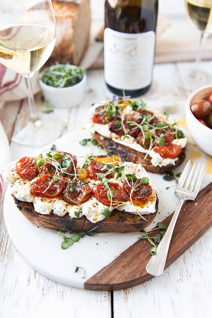 two pieces of bread with tomatoes and goat cheese on it next to a glass of wine