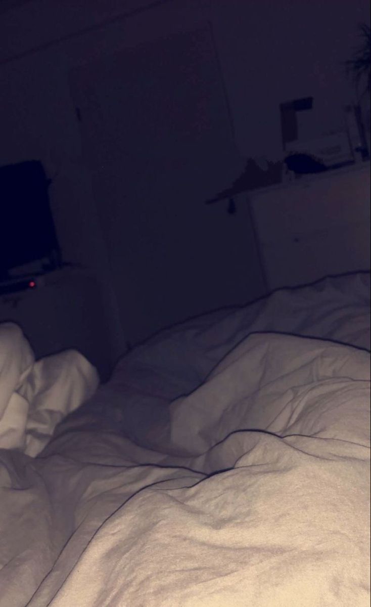 an unmade bed in a dark room with white sheets and blankets on top of it