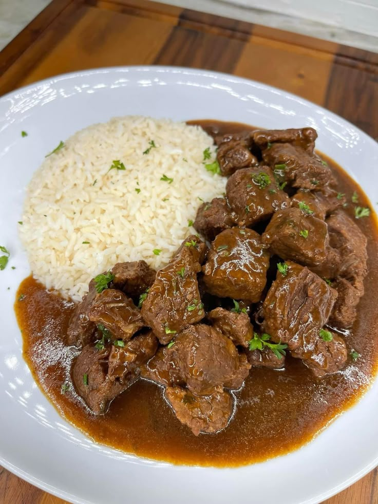 a white plate topped with meat and rice on top of a wooden table next to a fork