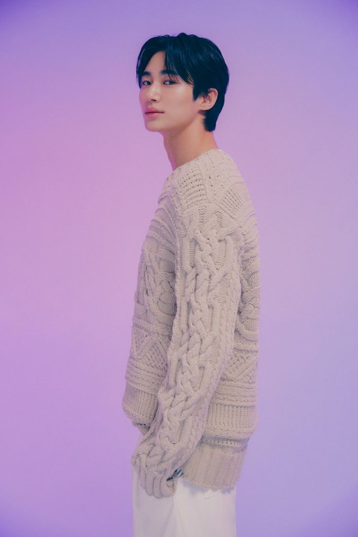 a woman with short black hair wearing a white sweater and jeans, standing in front of a purple background