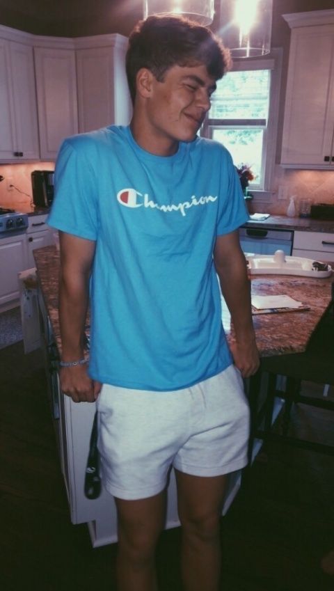 a young man standing in front of a kitchen counter wearing white shorts and a blue champion t - shirt