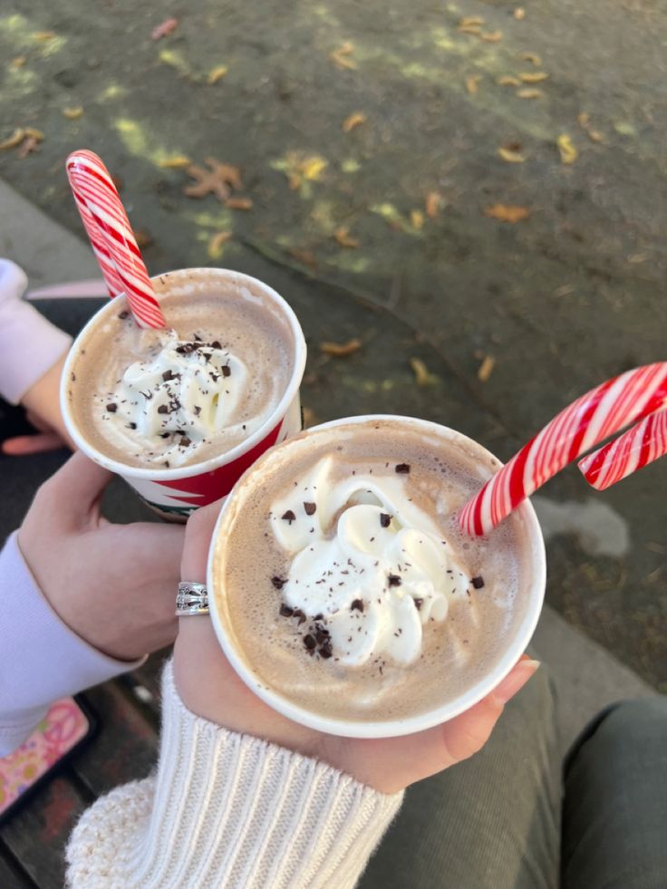 two people are holding cups with hot chocolate and candy canes