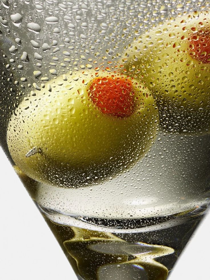 two olives in a martini glass with water droplets on the bottom and red dots