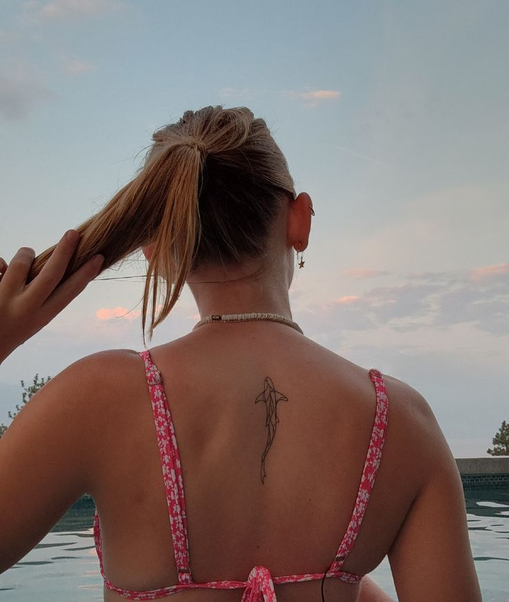 a woman with a tattoo on her back standing in front of a pool and looking at the water