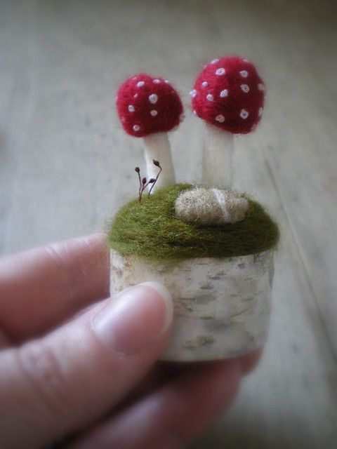 a hand holding a tiny mushroom with two red mushrooms on it's top and one white mushroom in the middle