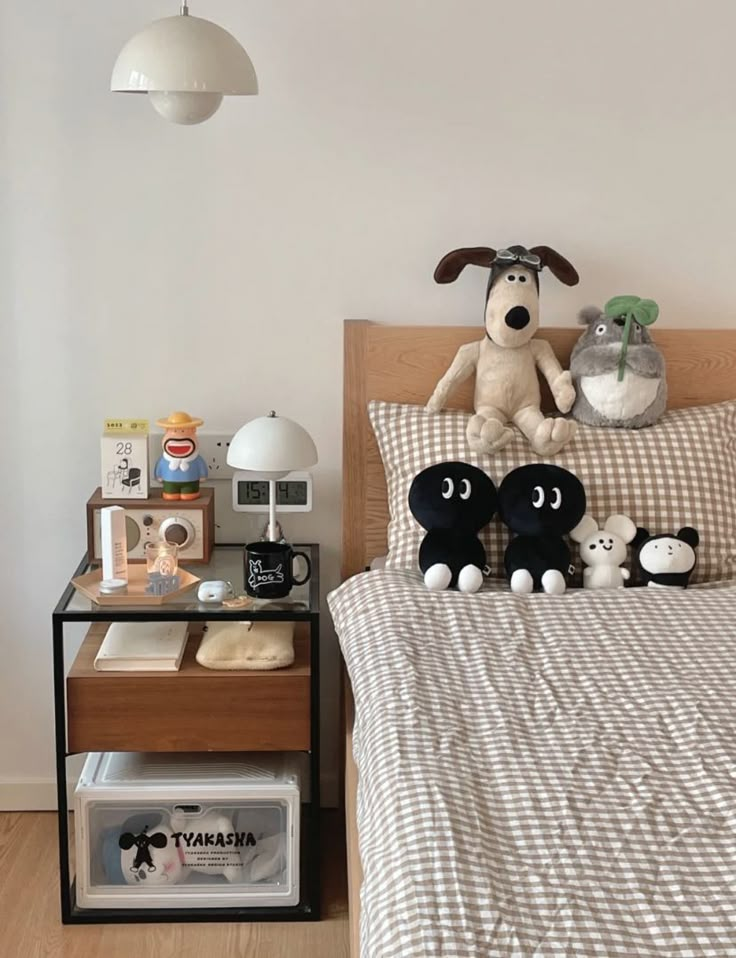 a bed topped with lots of stuffed animals next to a night stand and lamp above it