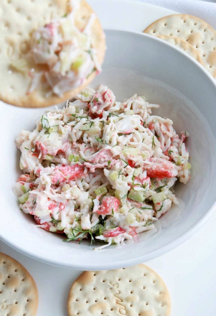 a white bowl filled with crab salad next to crackers