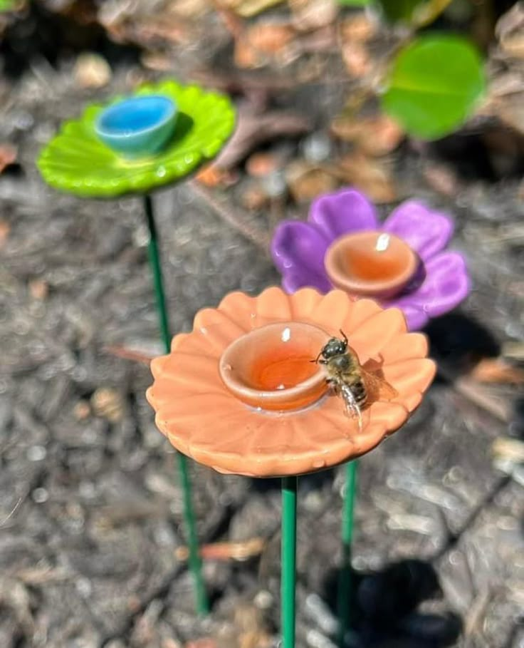 two flower shaped vases sitting on top of each other in the dirt next to flowers