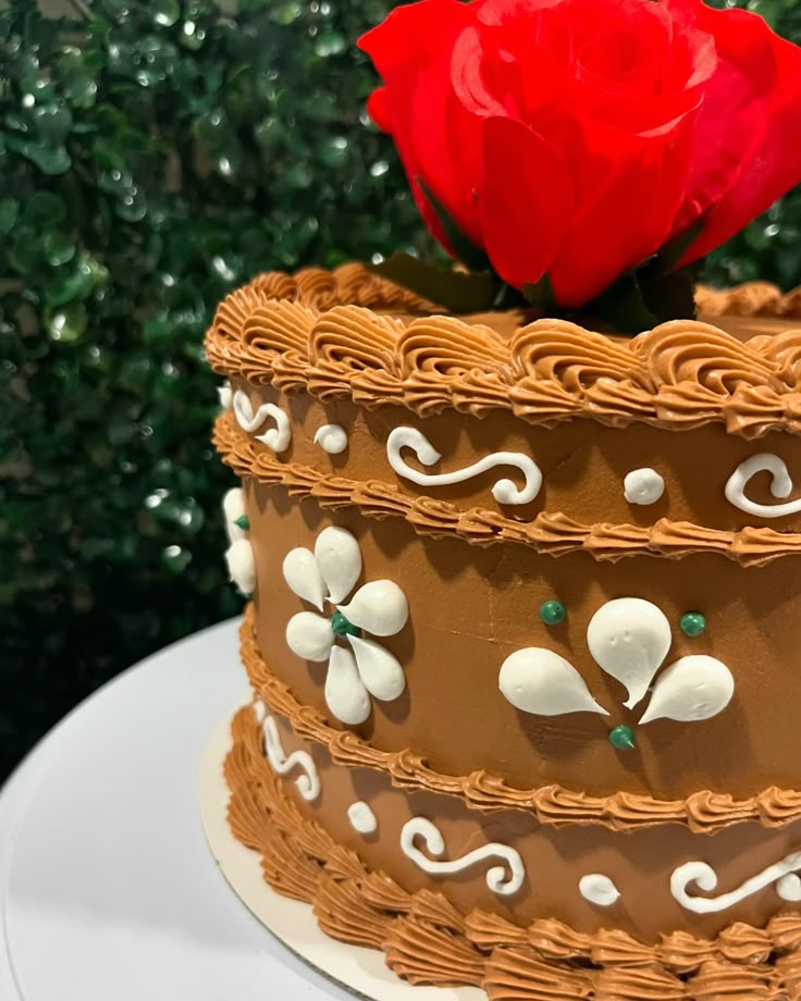 a decorated cake with a single red rose sitting on it's top layer and the icing is brown