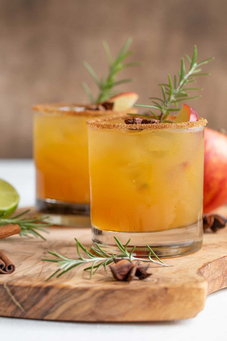 two glasses filled with orange juice and garnished with rosemary on a cutting board