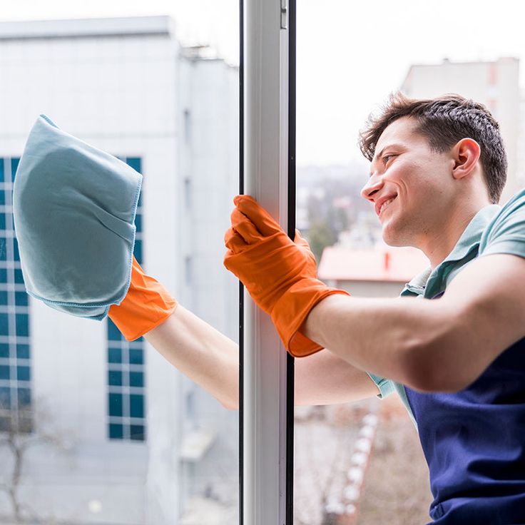 a man in blue shirt and orange gloves cleaning window glass with mitts on it