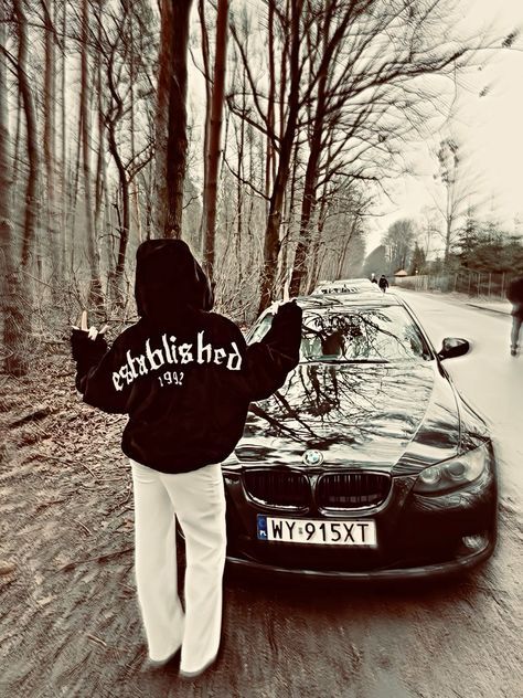 a person standing next to a parked car on a road in front of some trees