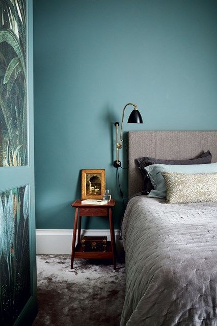 a bed room with a neatly made bed next to a blue wall and a painting on the wall