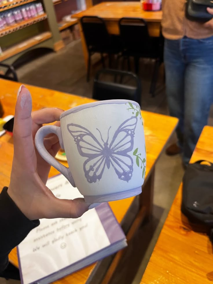 a person holding a coffee cup with a butterfly painted on it in the middle of a library