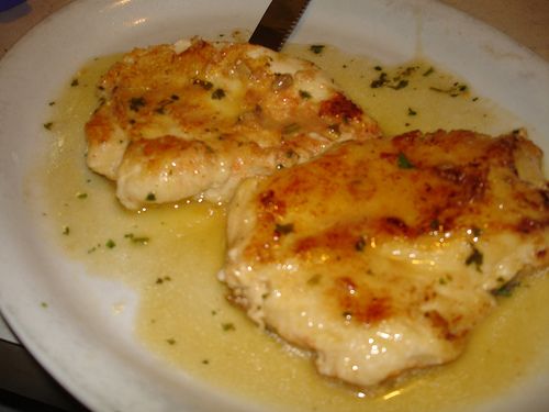 two pieces of chicken sitting on top of a white plate next to a knife and fork