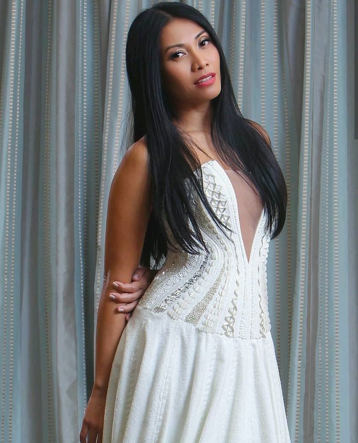 a woman in a white dress standing next to a curtain with her hands on her hips