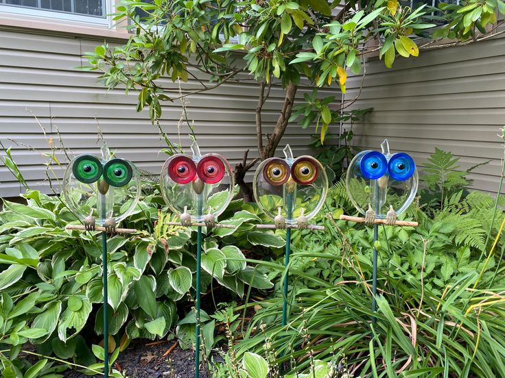 four colorful glass eyes sitting on top of metal poles in front of some bushes and trees