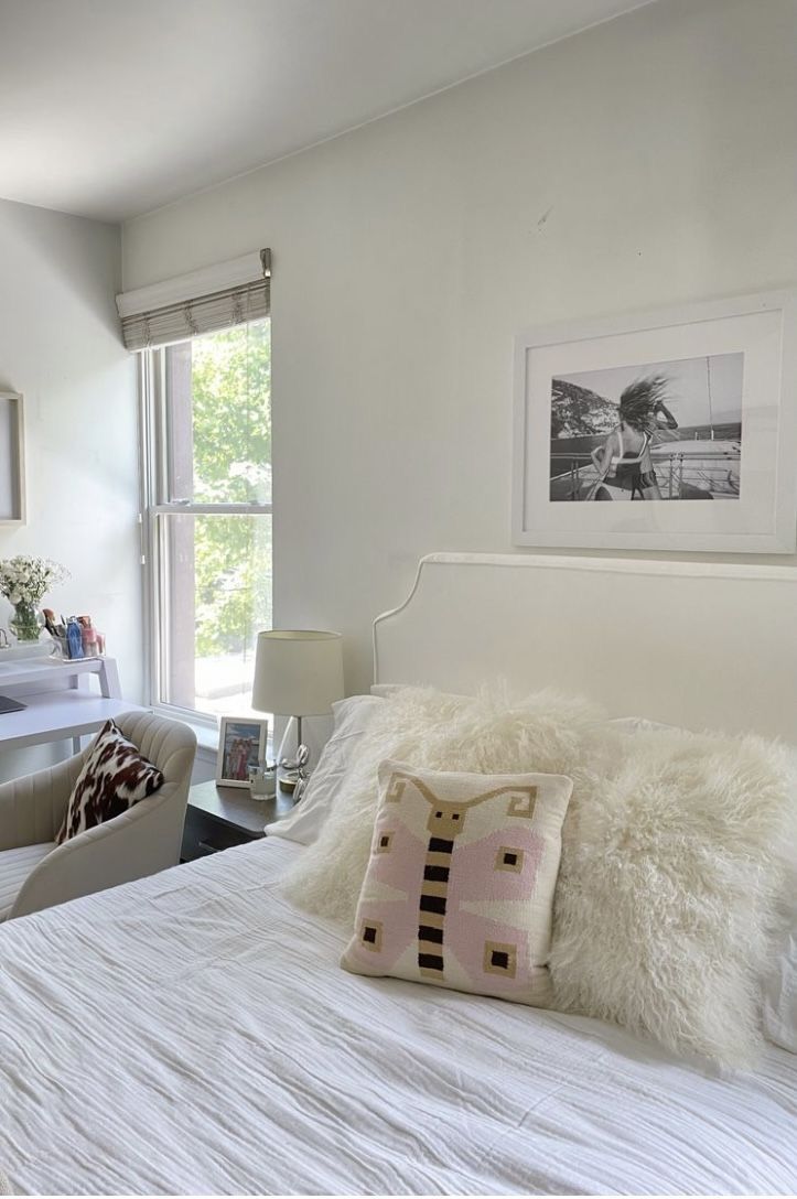 a bedroom with white bedding and pictures on the wall above it, along with two chairs