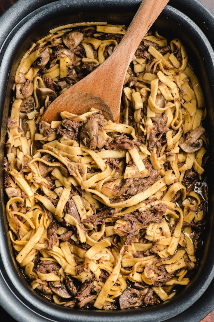 a wooden spoon in a pot filled with pasta and beef sauce on top of a table